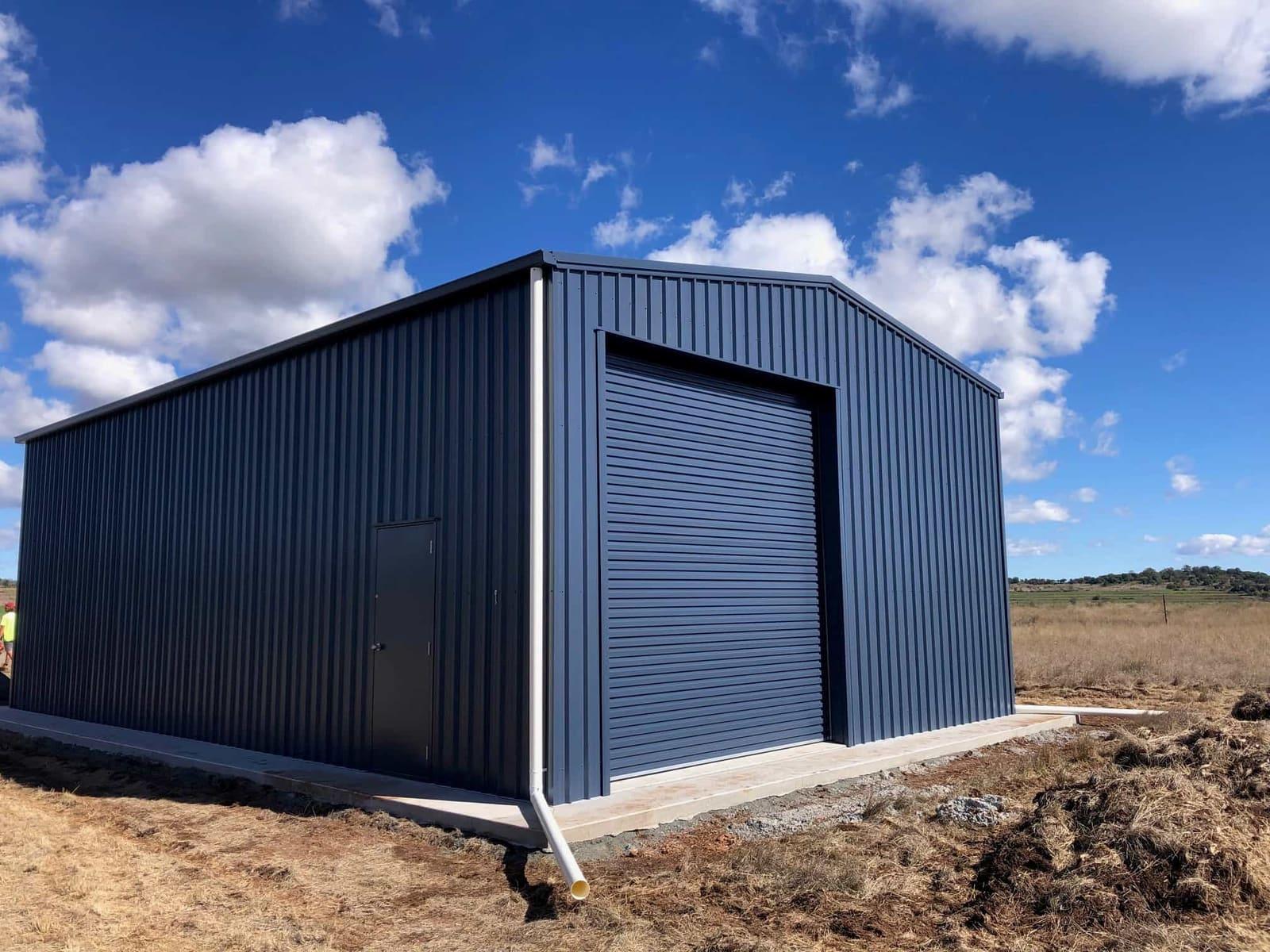 Tall navy steel shed with a high roller door on a rural block under a wide sky